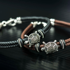 BRACCIALE IN CAUCIU’ INTRECCIATO NERO O MARRONE ED INSERTO CENTRALE TARTARUGA IN ARGENTO 925